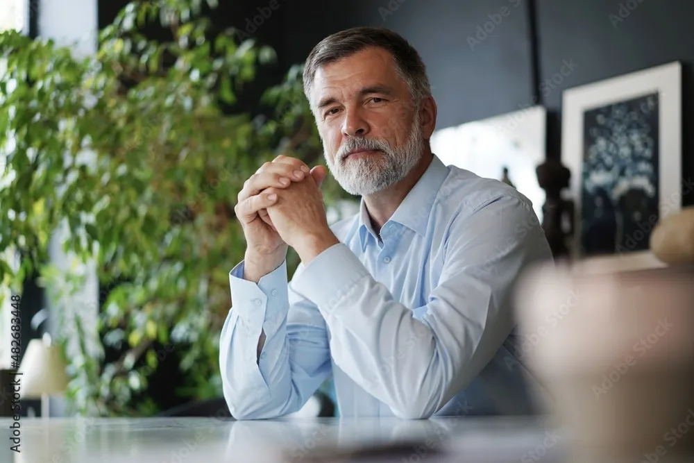 Mature professional businessman looking at camera and smiling. Confident entrepreneur, leader, manager sitting in office