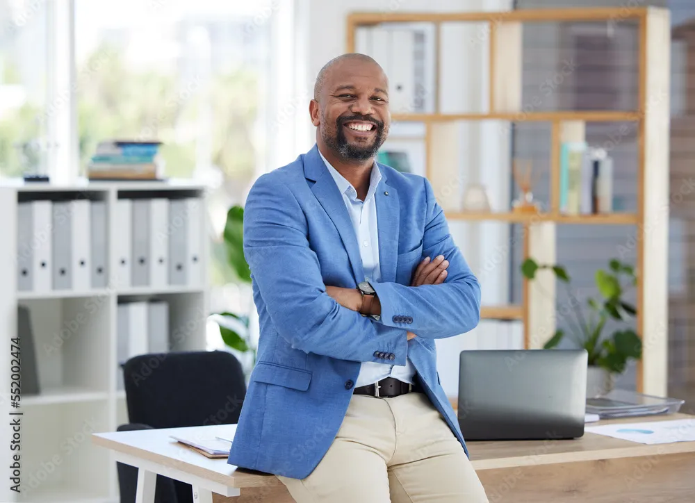 Success, corporate leadership and portrait of black man sitting on desk in modern office for startup. Management, marketing ceo and happy male entrepreneur with business vision in creative workplace
